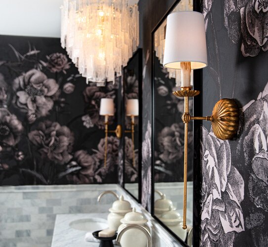 Antique gold leaf sconce in front of a black mirror with a glass chandelier above