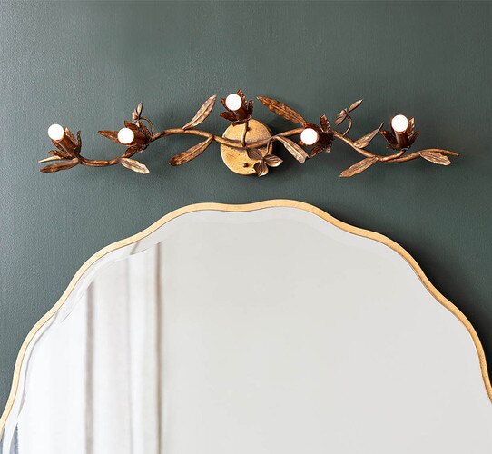 Linear gold flower sconce with light bulbs in the middle of the pedals above a gold mirror