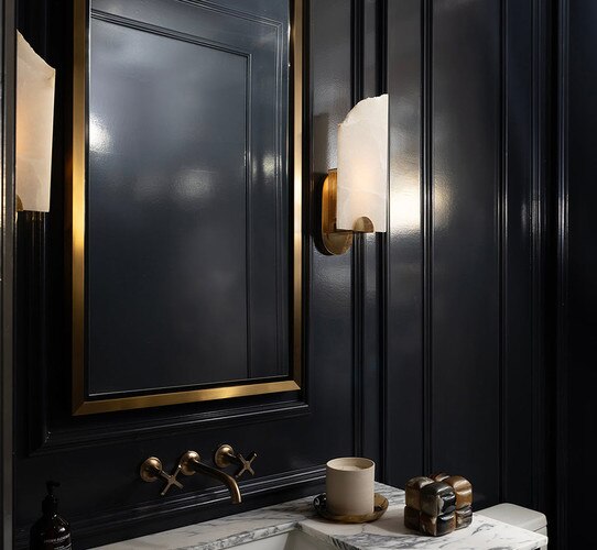 Alabaster wall sconces flanking a gold mirror in a black bathroom