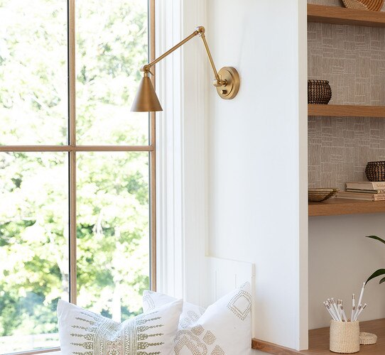 Brass task sconce above a reading nook with white pillows
