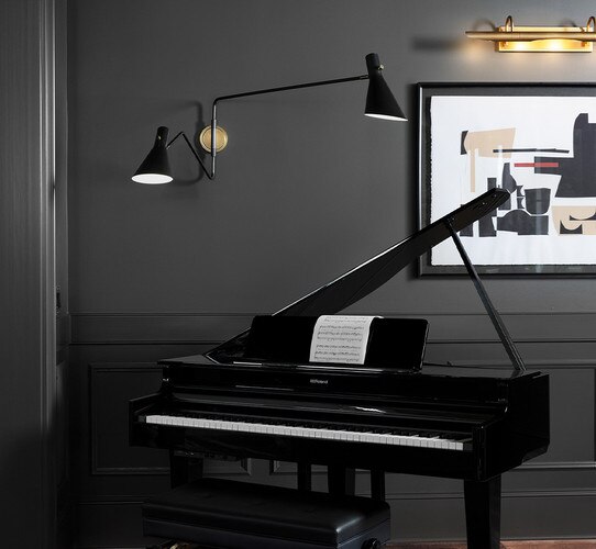Brass and black double armed task sconce above a small black piano
