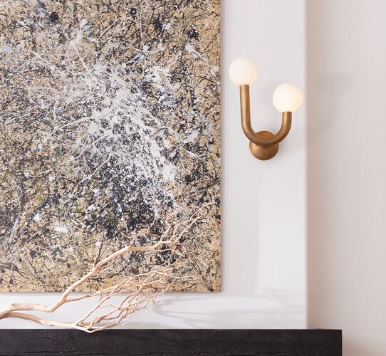 Double armed brass wall sconce next to an abstract painting of white and black splotches
