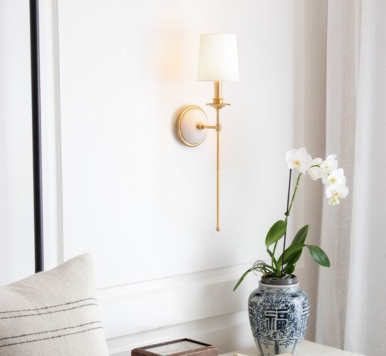 Thin traditional wall sconce with an alabaster base above a nightstand with decor