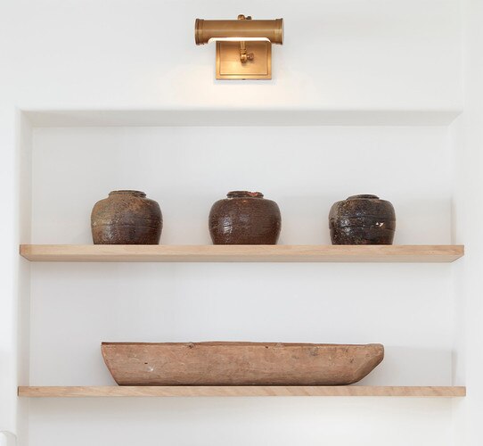 Small brass picture light above a shelf with three brown ceramic pots spaced evenly