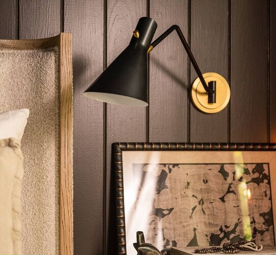Black and brass single arm sconce on a black wall