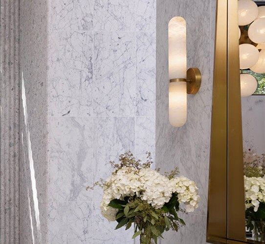 Alabaster wall sconce with a brass band in the middle next to a brass mirror
