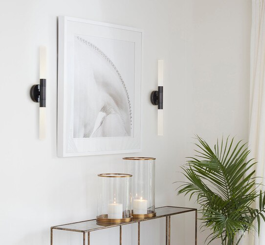 Bronze sconce with double vertical lights flanking a white picture frame