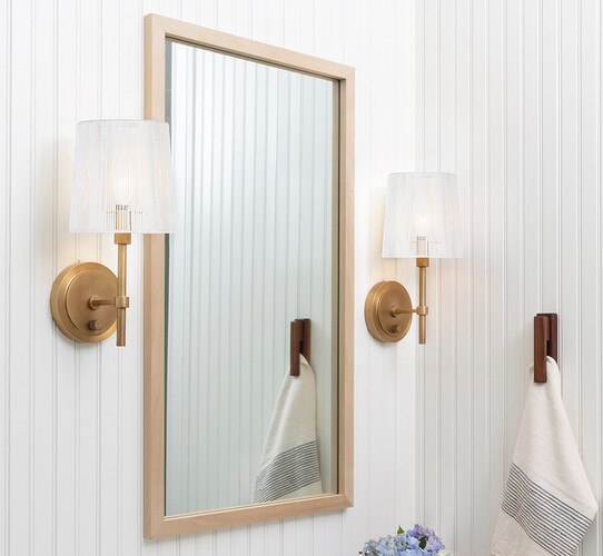 Brass sconce with plastic shade flanking a wooden mirror