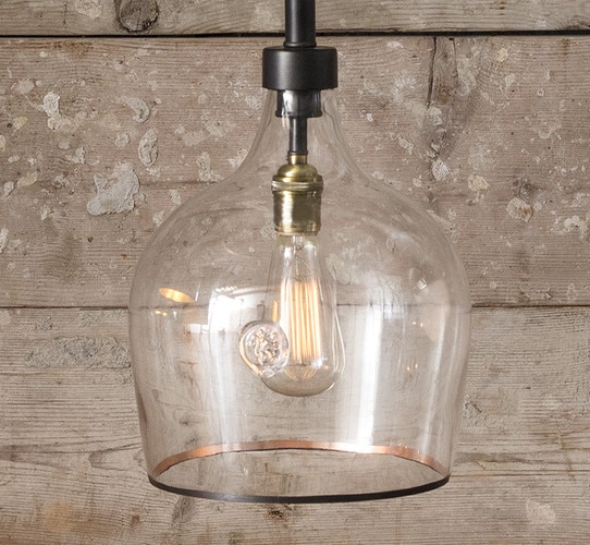 Clear glass pendant with brass lip in front of a worn wood wall