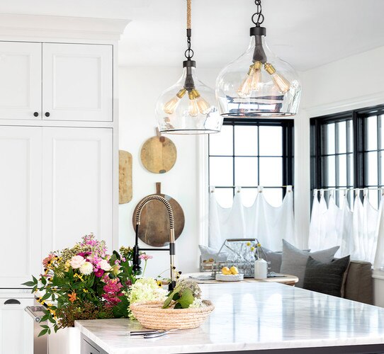 Large glass pendant with three sockets above a marble kitchen island with flowers in the sink