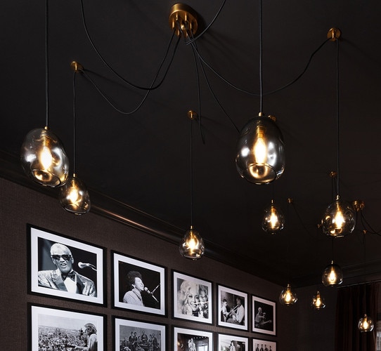 Large glass chandelier with multiple cords and hanging lights in front of a picture wall