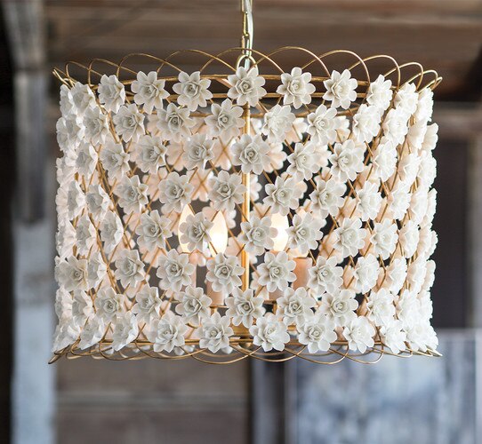 Gold and ceramic flower cage chandelier in front of a blurry wood and metal wall