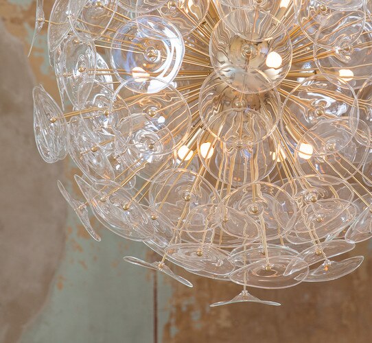 Clear and gold chandelier with poppy-like glass in front of a patinaed wall