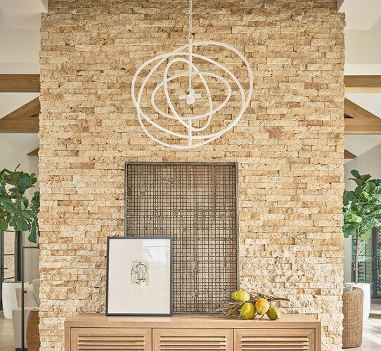 White circular rattan chandelier above a console table with plants and paintings