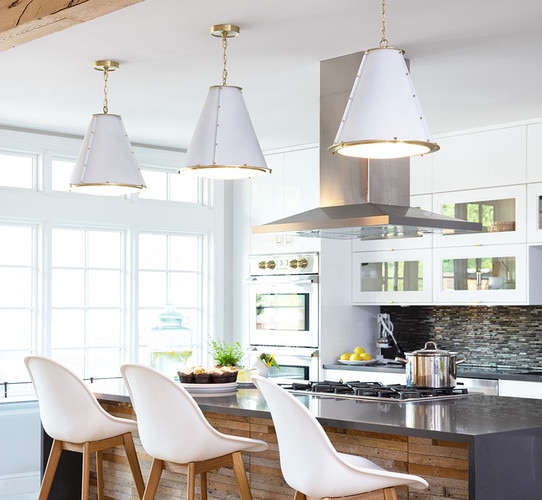 Three white and brass chandeliers above a marble and wood kitchen island