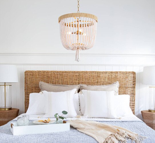 White wood beaded chandelier above a rattan bed with a tray of food