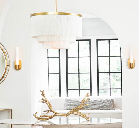 White and brass fringe chandelier above a marble table in a foyer