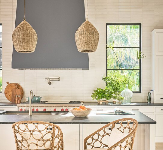 Two rattan pendant lights above a concrete kitchen island with rattan chairs