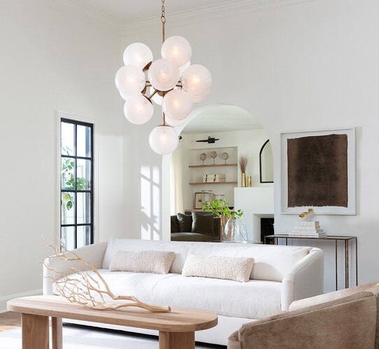 Milk glass and brass chandelier above a wooden nightstand and white couch