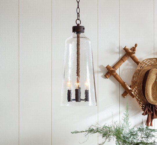 Hammered glass pendant with three black socets in front of a white shiplap wall