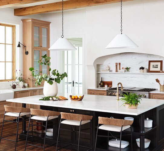 Two large concrete pendants above a large white island with chairs and plants