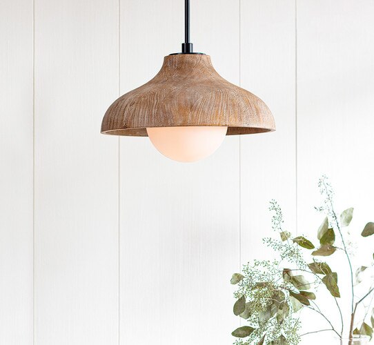 Natural wood pendant with protruding glass shade above a vase of foliage