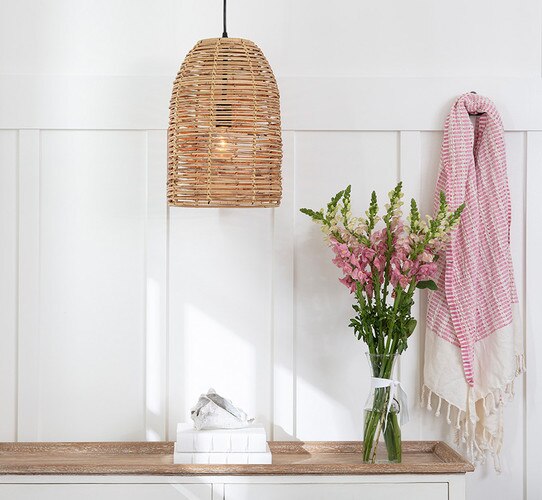 Wicker pendant light above a wood console table with flowers and books