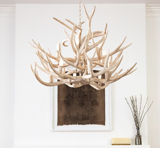 Tiered antler chandelier above a fireplace with a picture frame above it