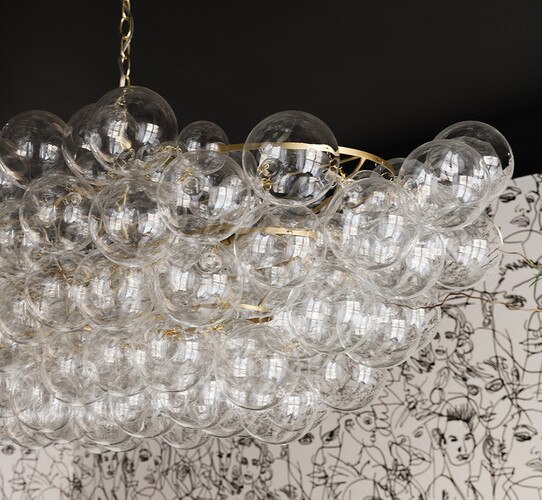 Brass and bubbled glass linear chandelier in front of abstract black and white wallpaper