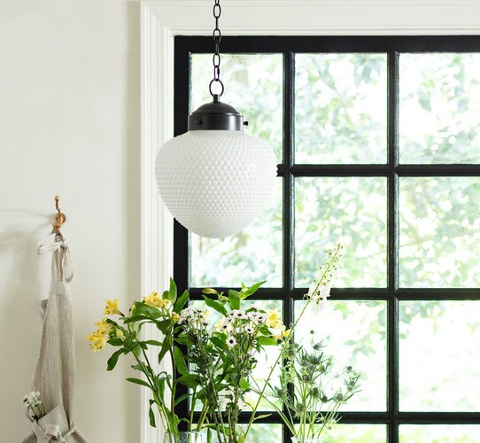 Milk glass pendant in front of a black window with flowers below it