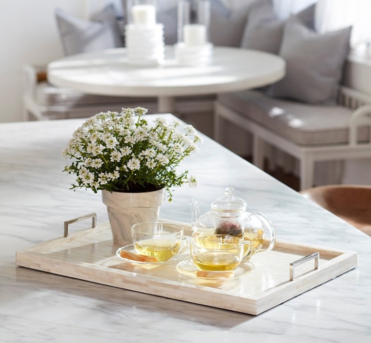 White bone tray with two tea cups, a kettle and potted flowers resting on top