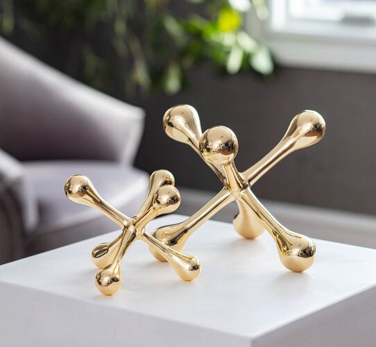 A small gold jack in front of a large gold jack on a white marble side table