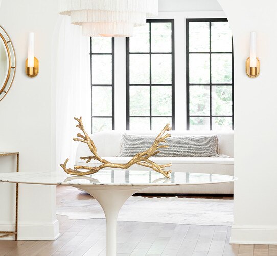 A gold metal branch on a circular white marble table in a foyer