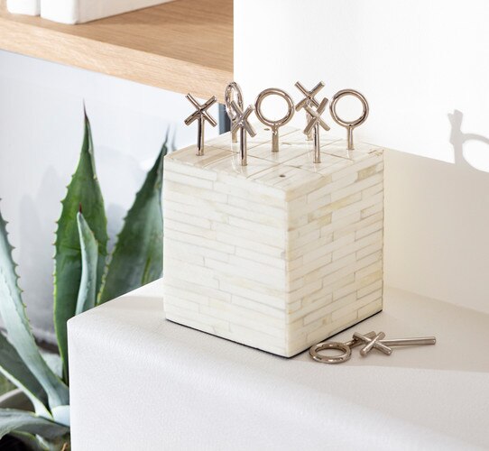 Square block of bone with polished nickel tic tac toe pieces protruding from the top