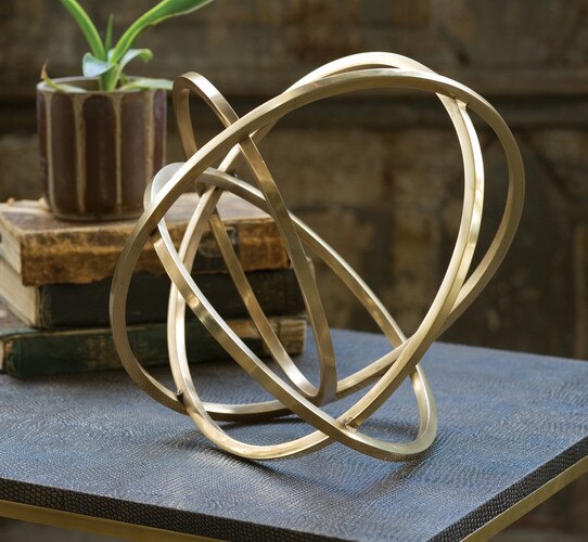 Brass ellipse sculpture next to three vintage books on a table