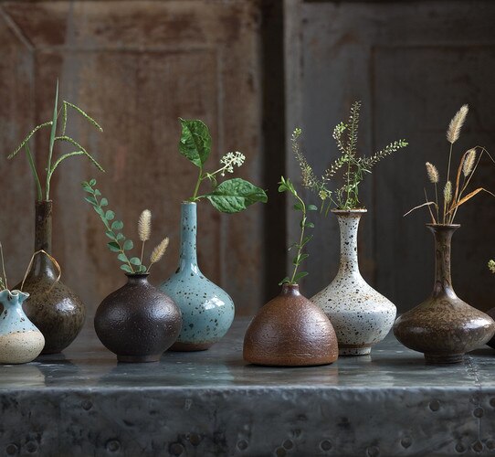Seven porcelain vases of different sizes and colors with stems in them