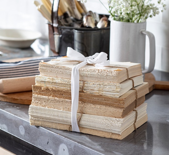 Unbound books wrapped in a bow on a steel countertop with a wood cutting board behind it