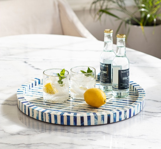 Bone and indigo round tray with two glasses of lemon tonic water atop beside a lemon