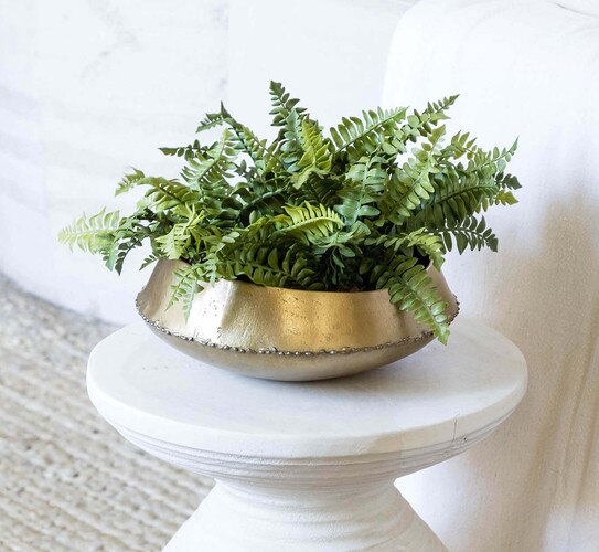 Large brass bowl with cut fern leaves inside, resting on a white pedestal