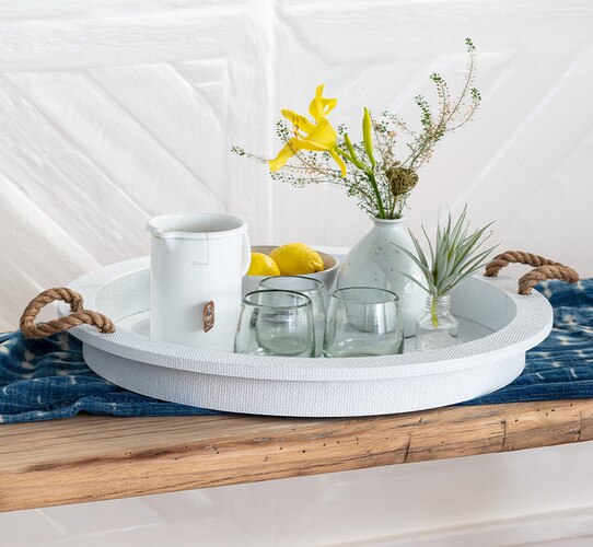 White serving tray with rope handles holding three clear glasses, a mug and a bowl of lemons
