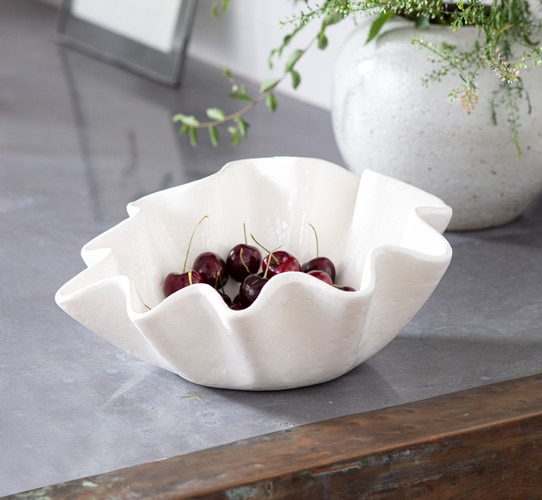 White ceramic ruffle bowl holding cherries on top of a metal table