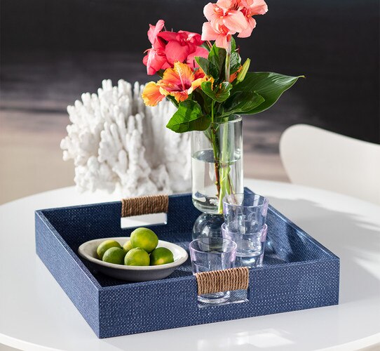 Blue tray holding a plate of limes three glasses and a vase of red and pink flowers