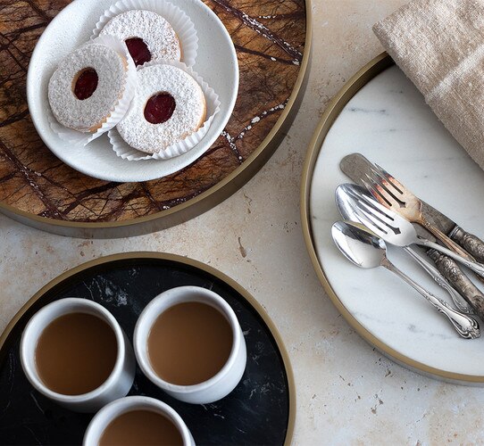 Three brass and marble trays holding mugs cookies and silverware