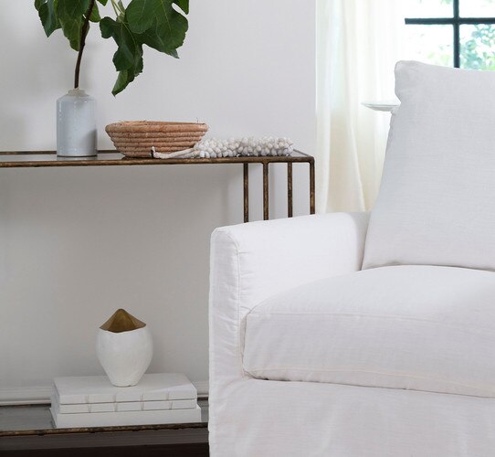 White chair in front of a console table with a white and gold vase, books and bowls