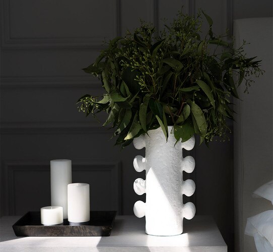 White metal vase holding green florals on a bedside table