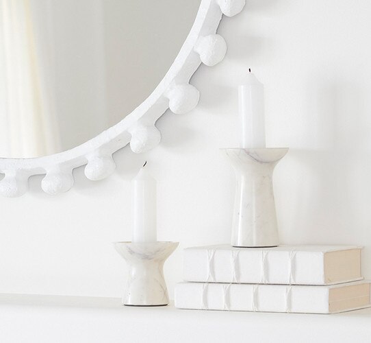 White marble candleholders resting on a mantle beside a stack of books