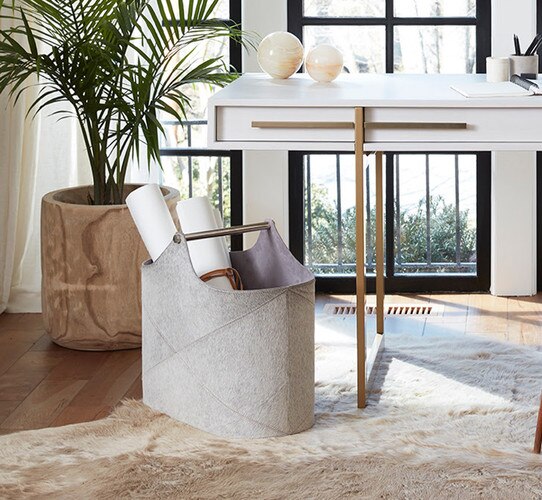 White and brass office desk beside a hair on hide basket with rolls of paper
