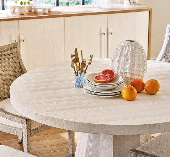 White dining table with plates silverware and fruit resting in the center
