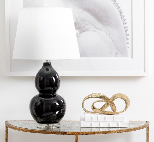 Gold console table with a black lamp and gold sculpture resting atop