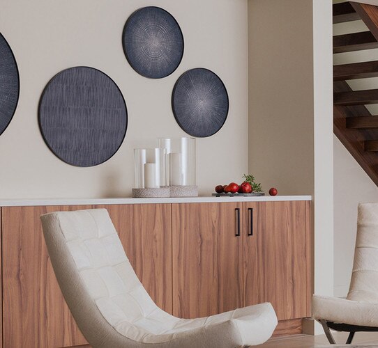 Sitting area with two white chairs and a wood shelving unit with two glass hurricanes on top